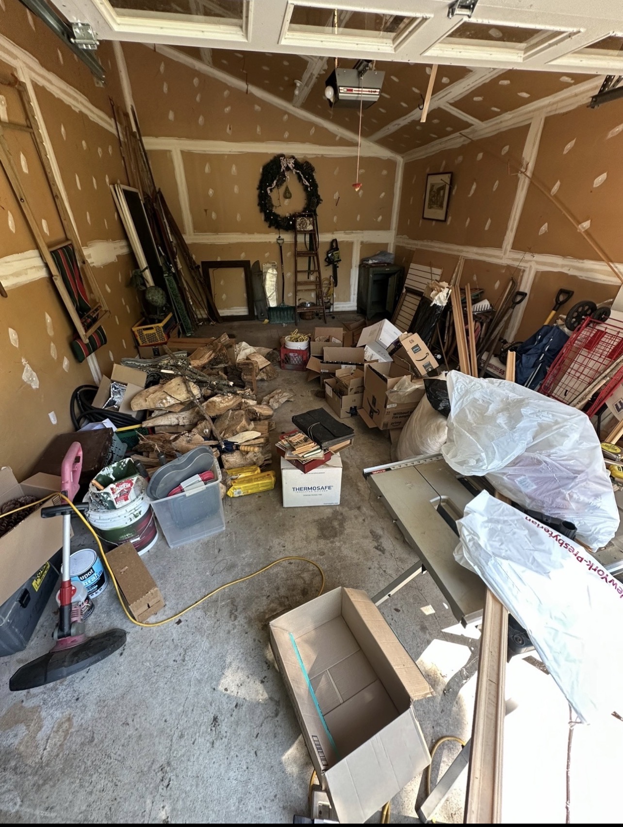 Cluttered garage floor before cleanout — boxes, firewood, and debris covering the floor